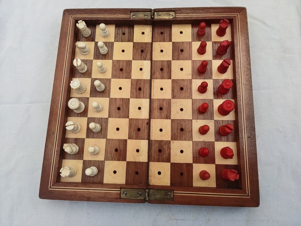 An open antique mahogany folding travelling chess board containing miniature carved red and natural white bone chess pieces fitted into individual pegged holes. View VII