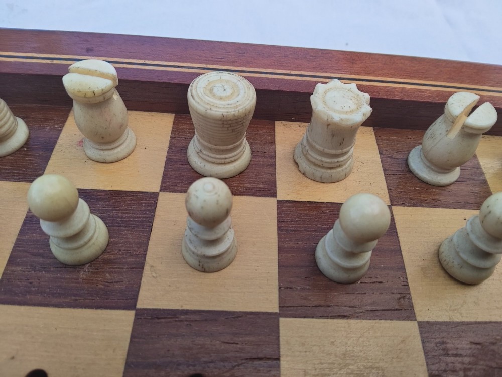 An open antique mahogany folding travelling chess board containing miniature carved red and natural white bone chess pieces fitted into individual pegged holes. View X