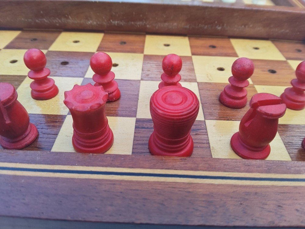 An open antique mahogany folding travelling chess board containing miniature carved red and natural white bone chess pieces fitted into individual pegged holes. View XI