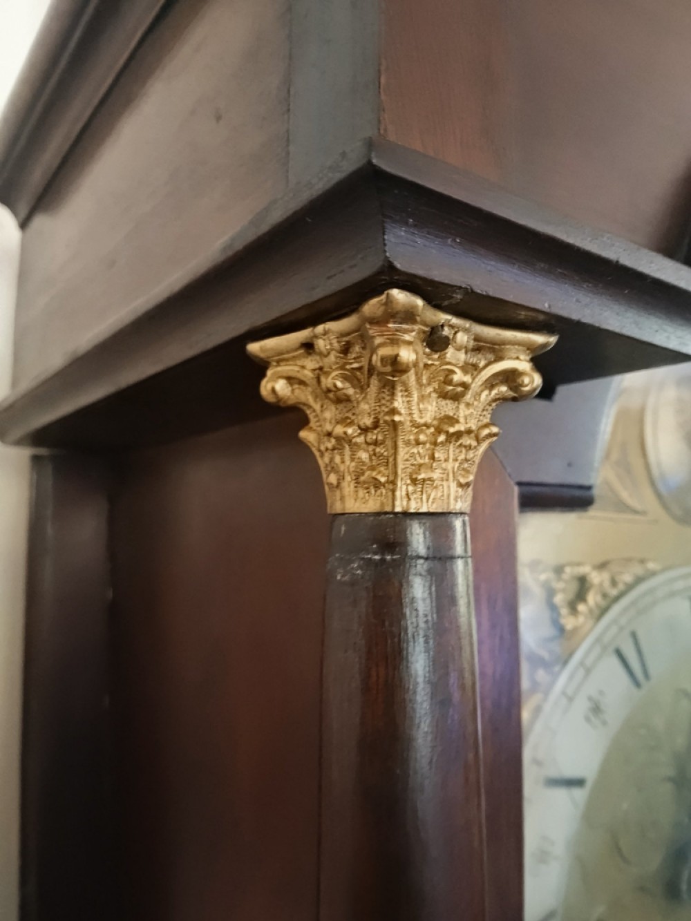 A slim dark mahogany longcase clock featuring a swan-neck pediment, brass dial with Roman numerals, and an arched trunk door. View IV