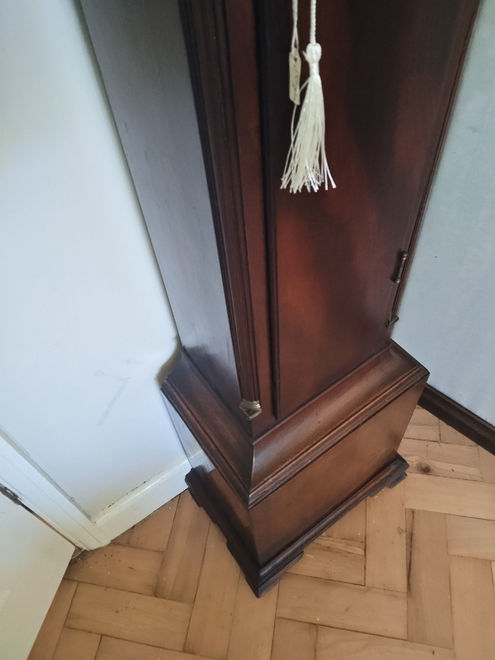 A slim dark mahogany longcase clock featuring a swan-neck pediment, brass dial with Roman numerals, and an arched trunk door. View VIII