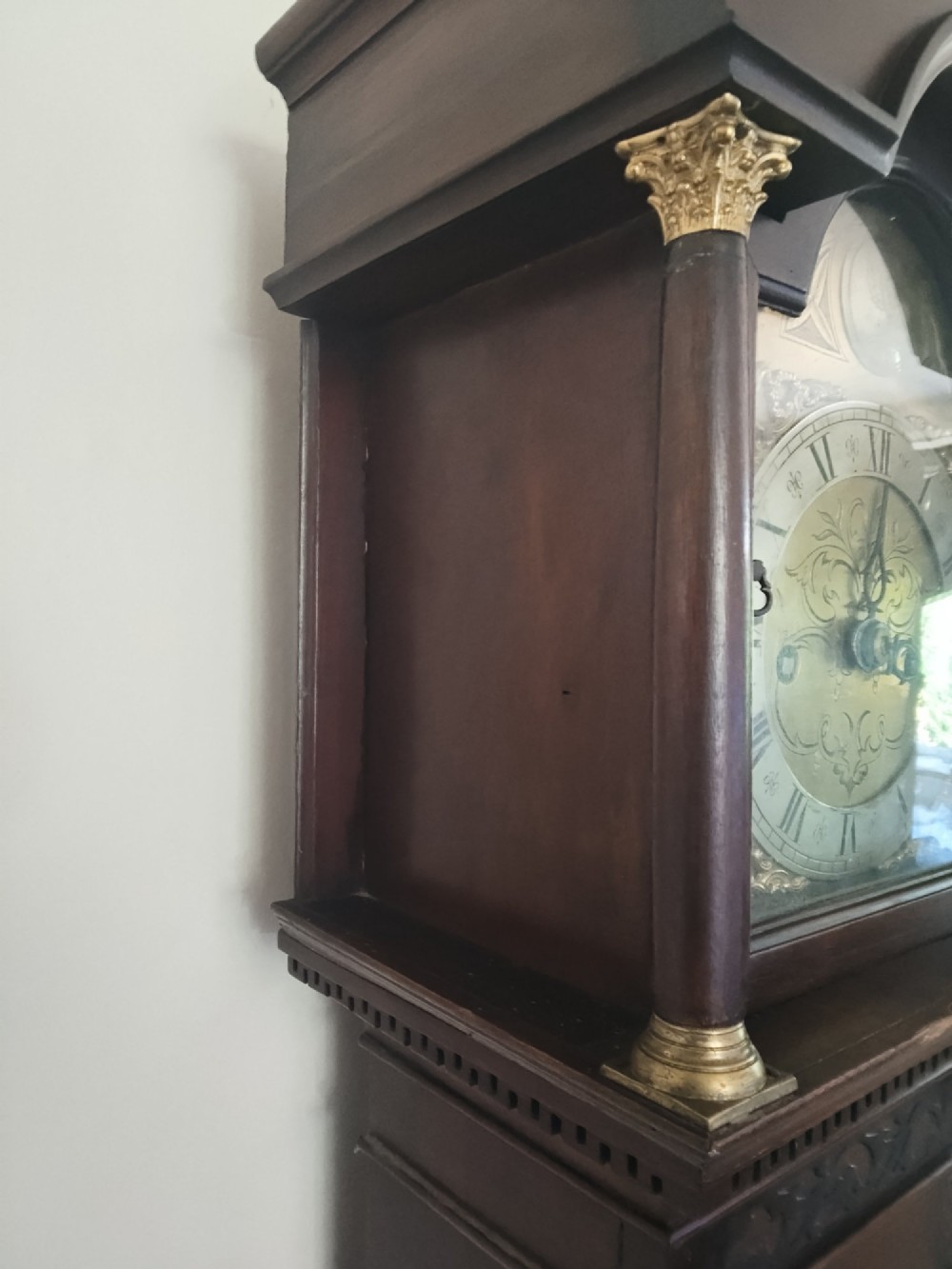 A slim dark mahogany longcase clock featuring a swan-neck pediment, brass dial with Roman numerals, and an arched trunk door. View IX