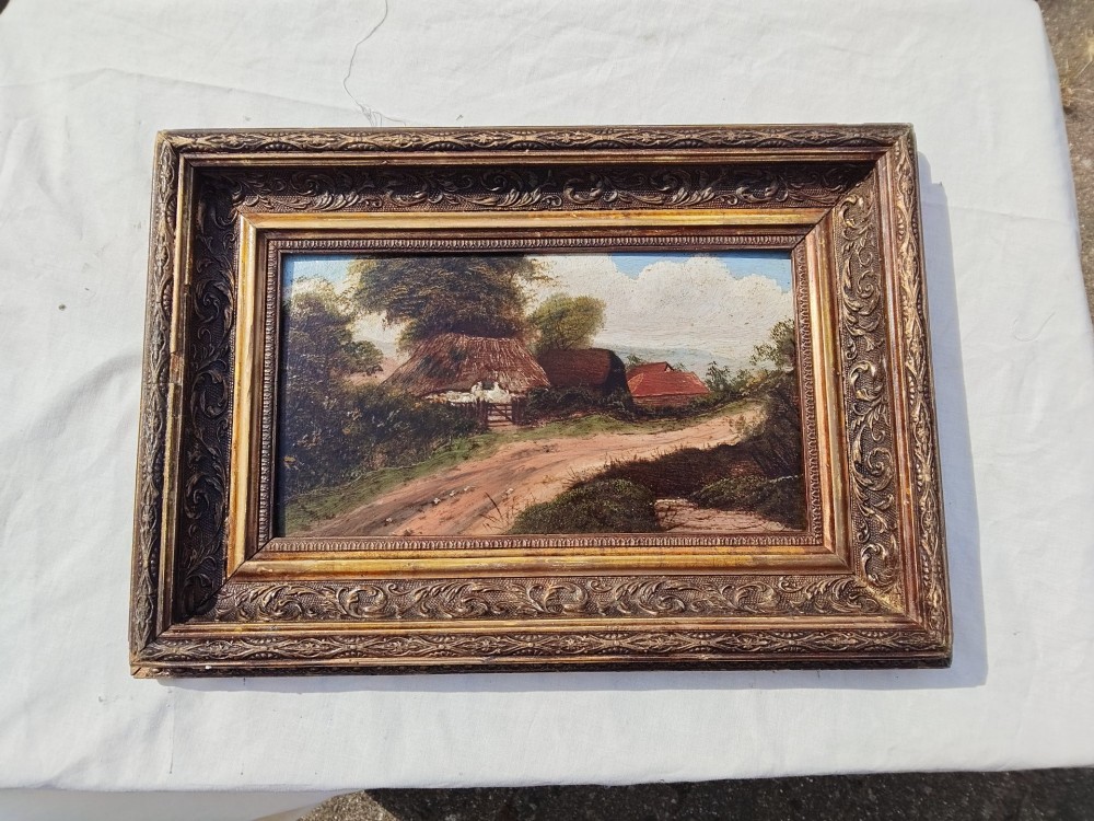 An antique oil painting on card depicting a rural English thatched cottage along a dirt path, set inside an ornate gilt frame. View VI