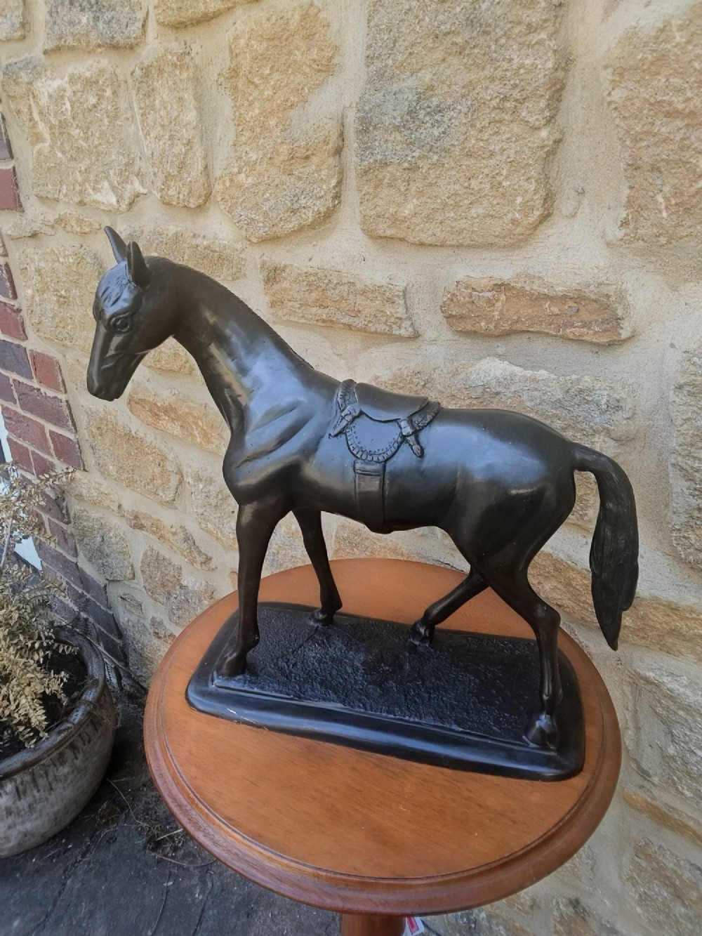 A dark brown cast bronze sculpture depicting a saddled standing horse positioned on an integral rectangular base. View III