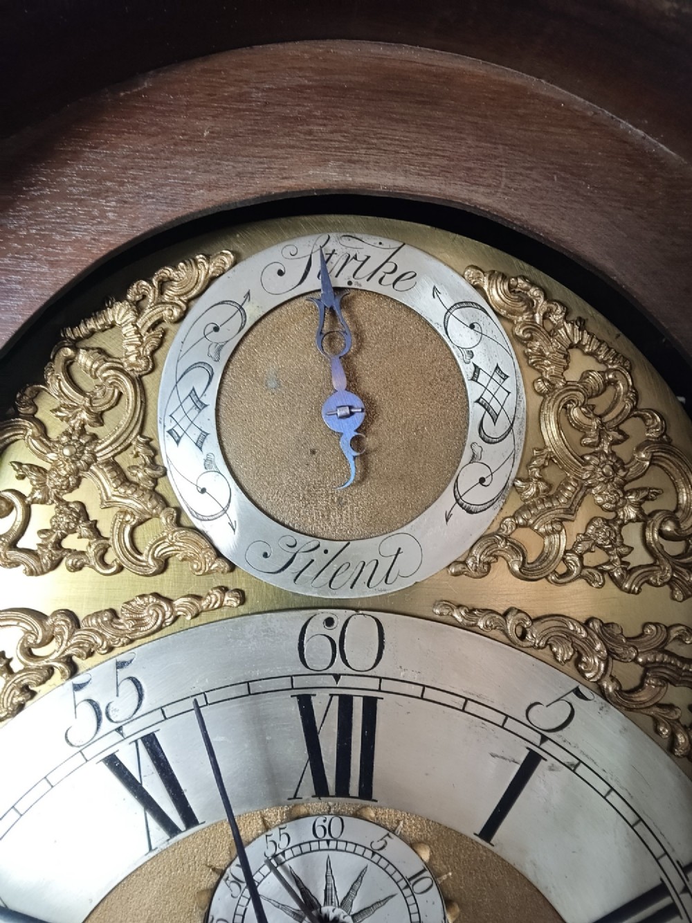 An antique Georgian longcase clock in dark mahogany featuring an arched hood and a brass dial with a strike-silent selector. View II