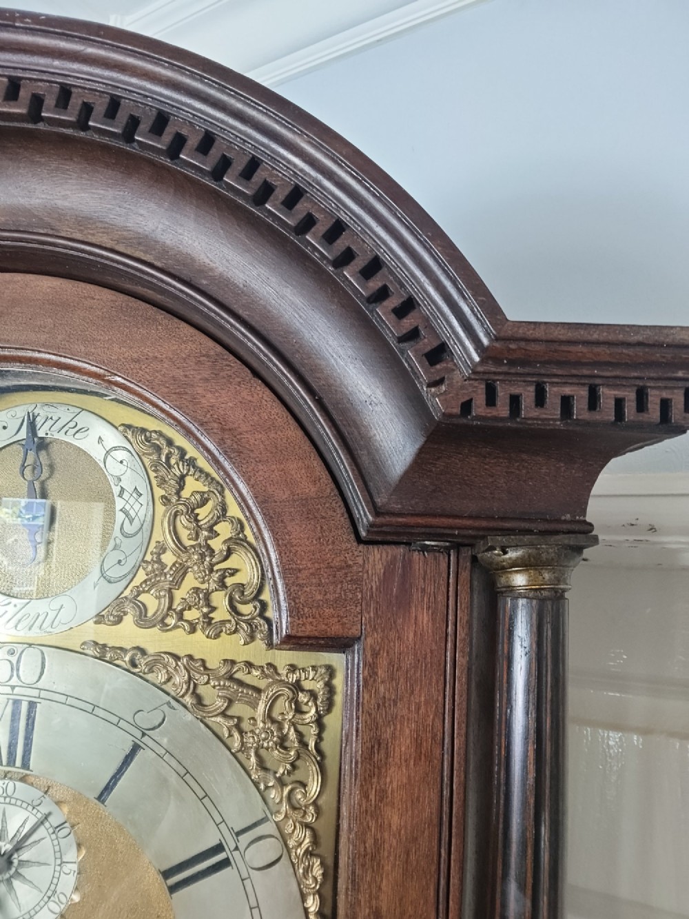 An antique Georgian longcase clock in dark mahogany featuring an arched hood and a brass dial with a strike-silent selector. View IV