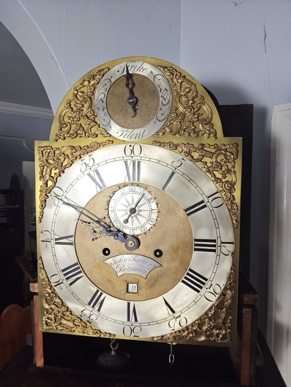 An antique Georgian longcase clock in dark mahogany featuring an arched hood and a brass dial with a strike-silent selector. View XII