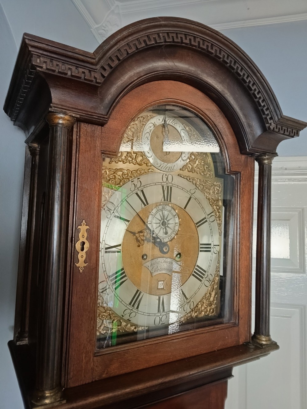 An antique Georgian longcase clock in dark mahogany featuring an arched hood and a brass dial with a strike-silent selector. View XIII