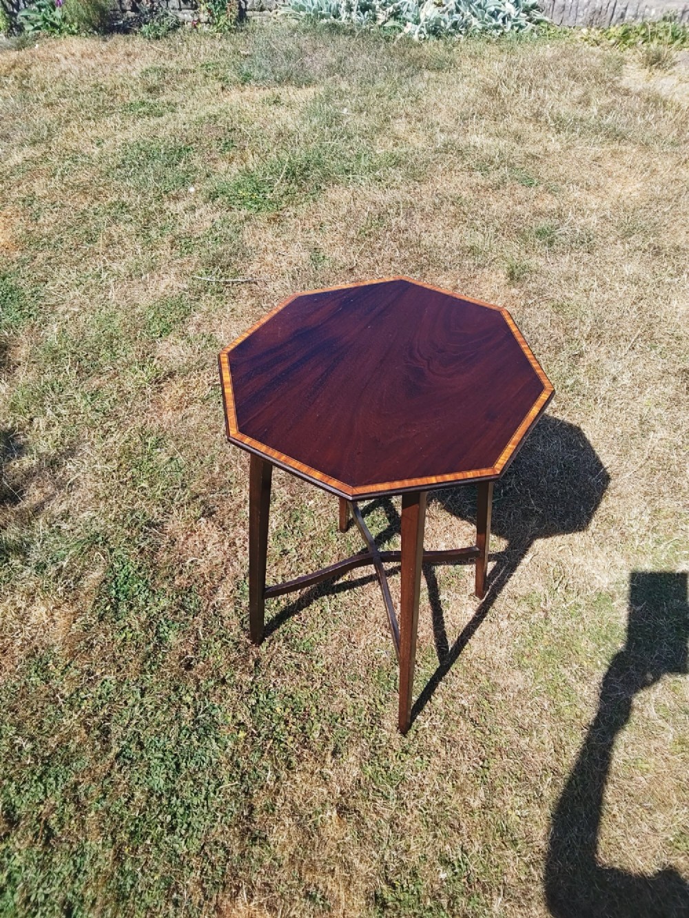 An octagonal dark mahogany side table featuring crossbanded timber inlay around the top surface and four tapered legs supported by an X-shaped stretcher.