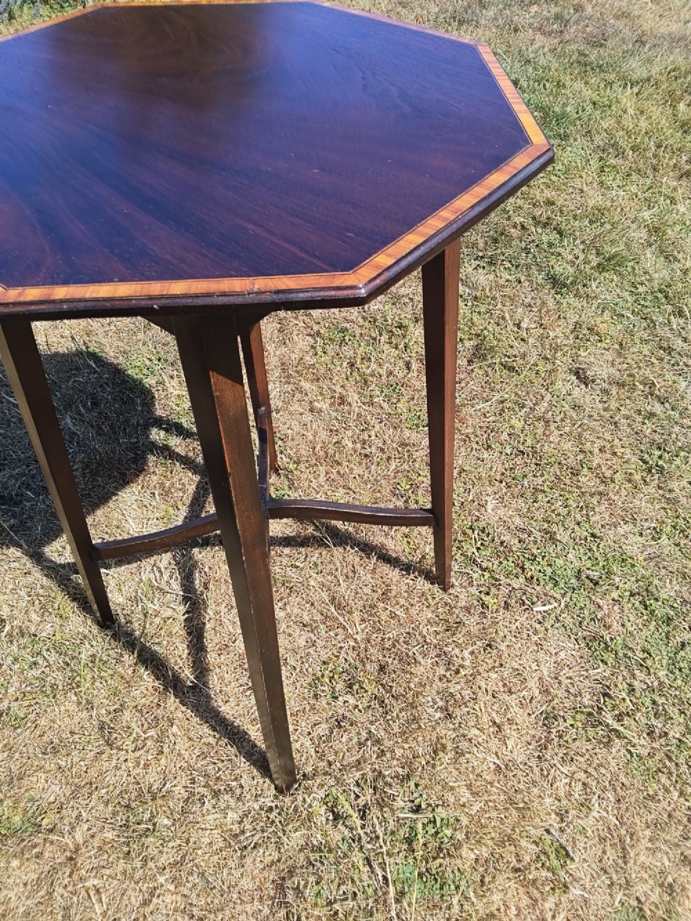 An octagonal dark mahogany side table featuring crossbanded timber inlay around the top surface and four tapered legs supported by an X-shaped stretcher. View IV