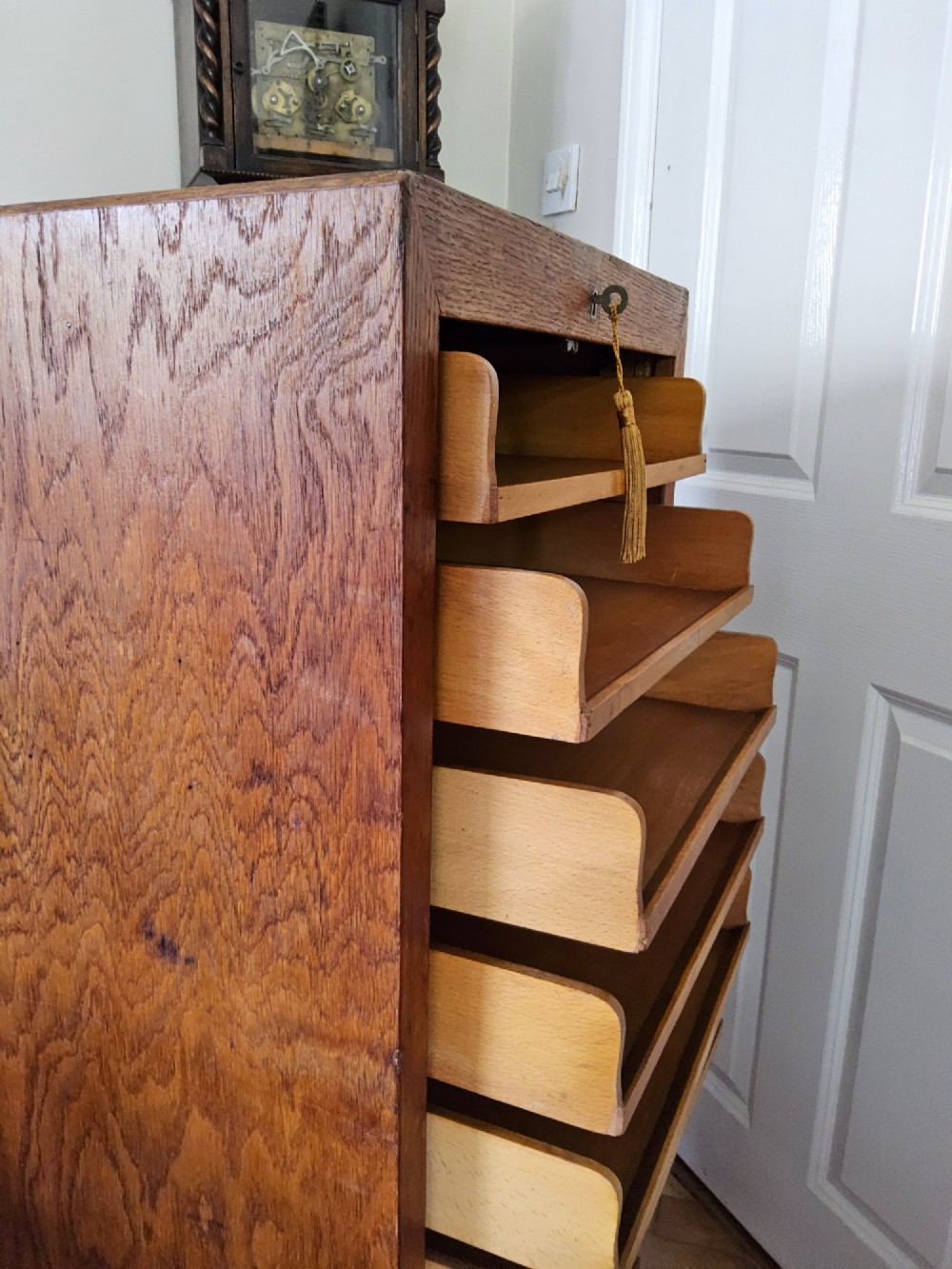 A tall oak tambour filing cabinet featuring a slatted wooden roll-front shutter door with a key inserted near the upper handle. View V