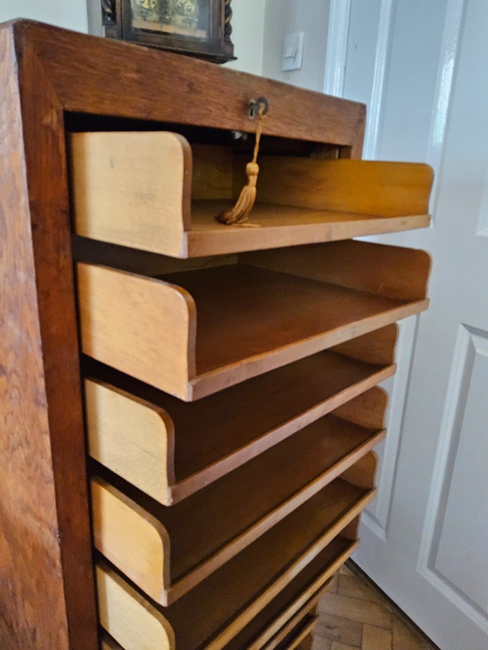 A tall oak tambour filing cabinet featuring a slatted wooden roll-front shutter door with a key inserted near the upper handle. View VI