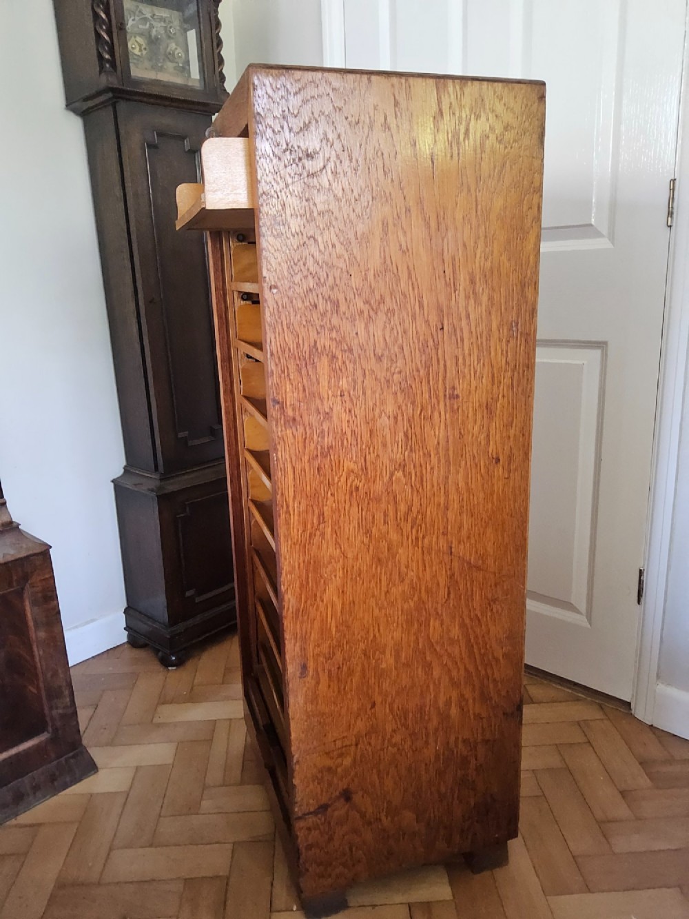 A tall oak tambour filing cabinet featuring a slatted wooden roll-front shutter door with a key inserted near the upper handle. View X