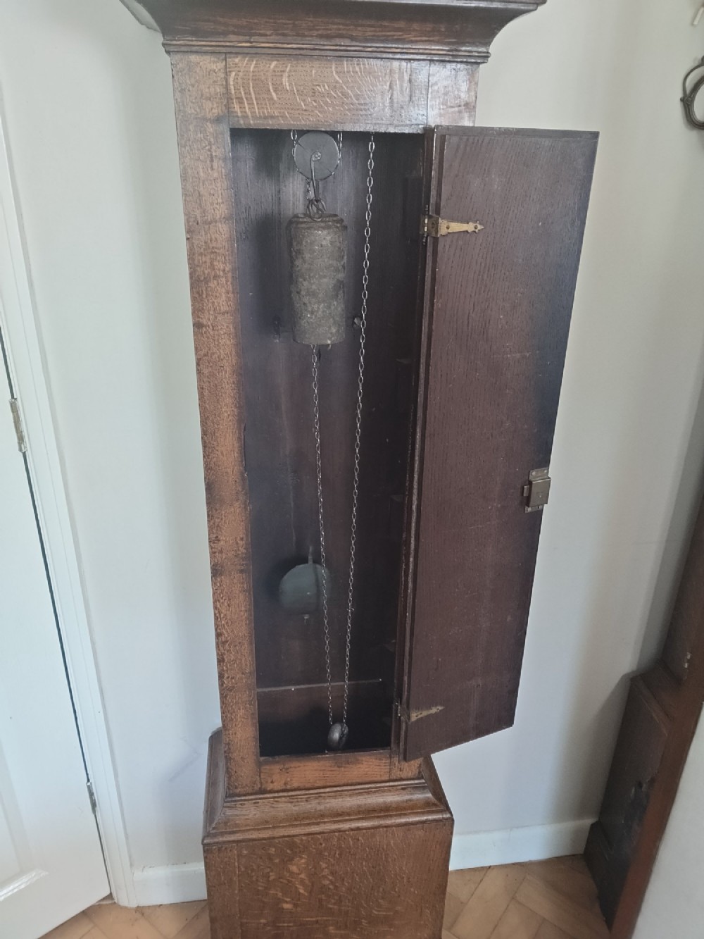 A freestanding Georgian oak longcase clock featuring a square brass dial, slender trunk door, turned hood columns, and a square plinth base. View VI