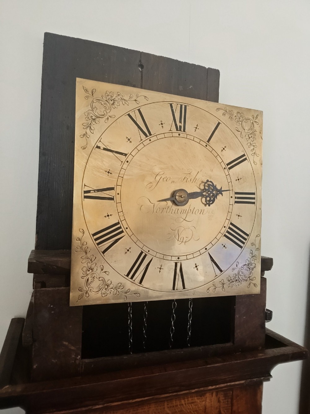 A freestanding Georgian oak longcase clock featuring a square brass dial, slender trunk door, turned hood columns, and a square plinth base. View IX