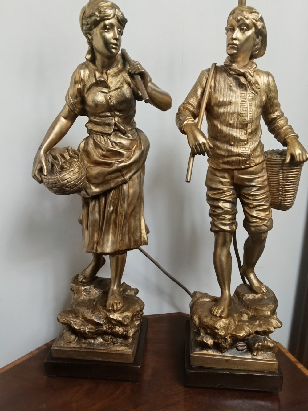 A pair of gold gilt metal table lamps depicting standing figures of French rustic workers mounted on square wooden bases. View VI