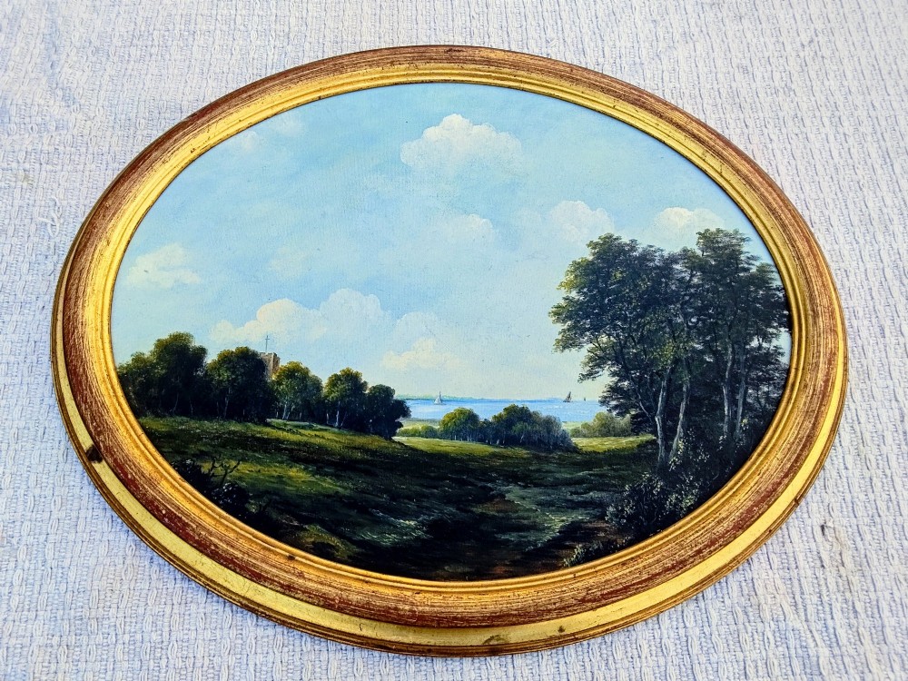 An oval oil painting depicting a grassy coastal landscape with trees, a distant church tower, and sailboats on the blue sea beneath a cloudy sky, encased in a gilt frame. View VII