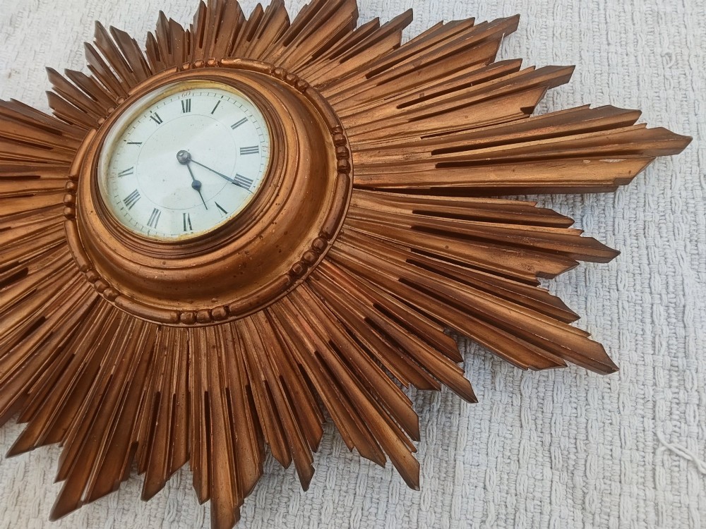 An early 20th-century giltwood starburst wall clock with carved radiating rays surrounding a circular white dial with Roman numerals. View II