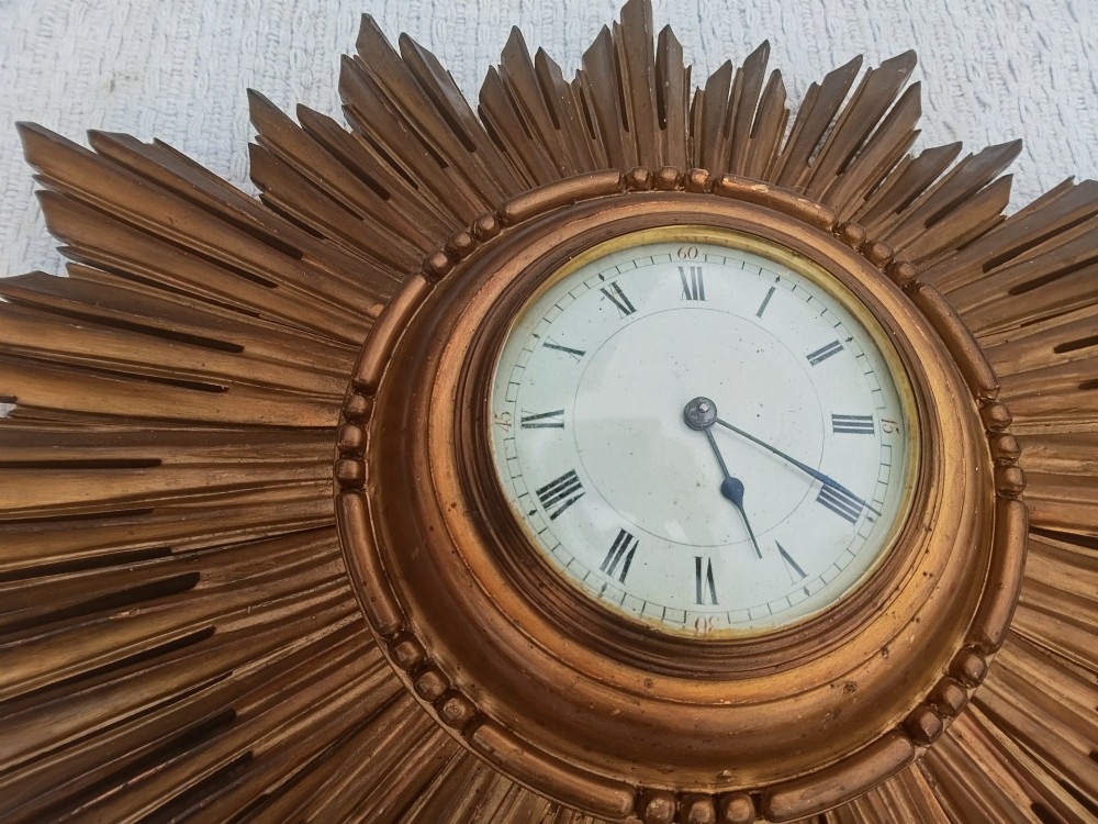 An early 20th-century giltwood starburst wall clock with carved radiating rays surrounding a circular white dial with Roman numerals. View III
