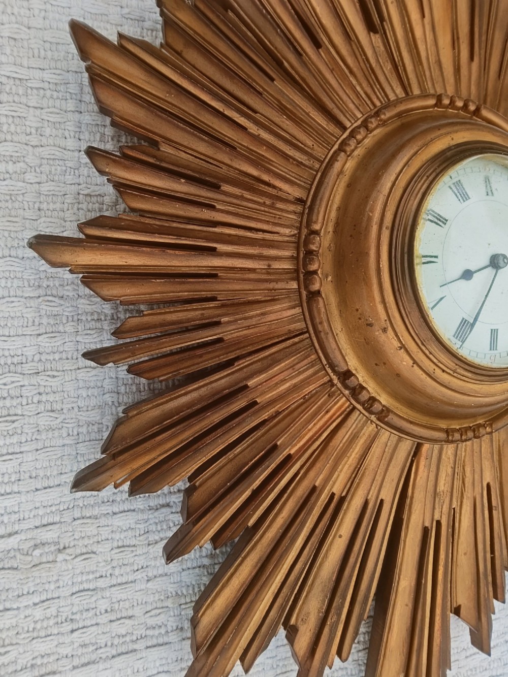 An early 20th-century giltwood starburst wall clock with carved radiating rays surrounding a circular white dial with Roman numerals. View IV