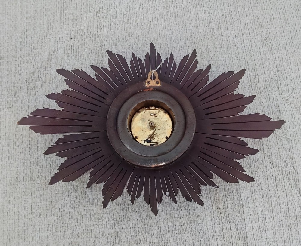 An early 20th-century giltwood starburst wall clock with carved radiating rays surrounding a circular white dial with Roman numerals. View VI