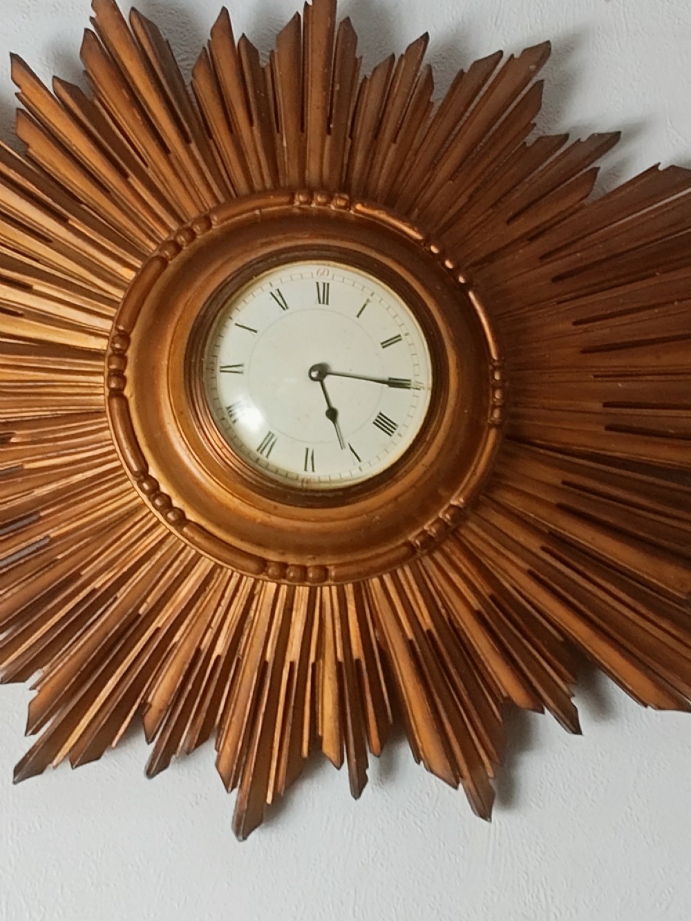 An early 20th-century giltwood starburst wall clock with carved radiating rays surrounding a circular white dial with Roman numerals. View VII