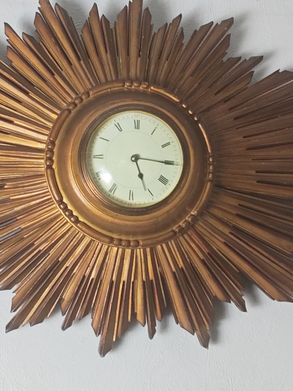 An early 20th-century giltwood starburst wall clock with carved radiating rays surrounding a circular white dial with Roman numerals. View VIII