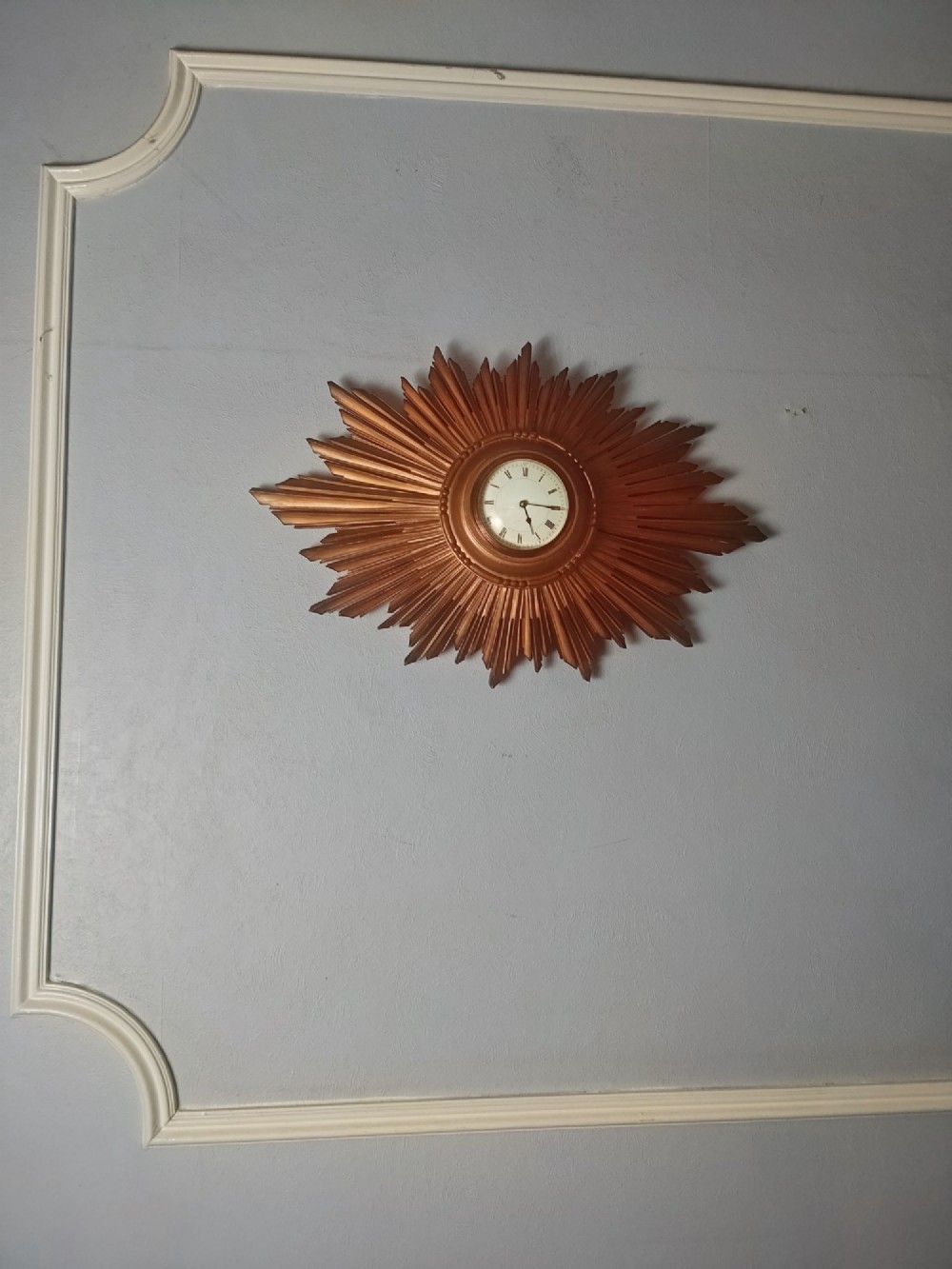An early 20th-century giltwood starburst wall clock with carved radiating rays surrounding a circular white dial with Roman numerals. View IX