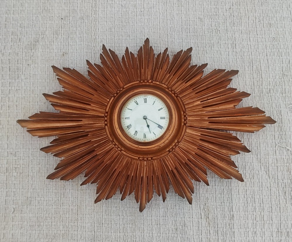 An early 20th-century giltwood starburst wall clock with carved radiating rays surrounding a circular white dial with Roman numerals. View X