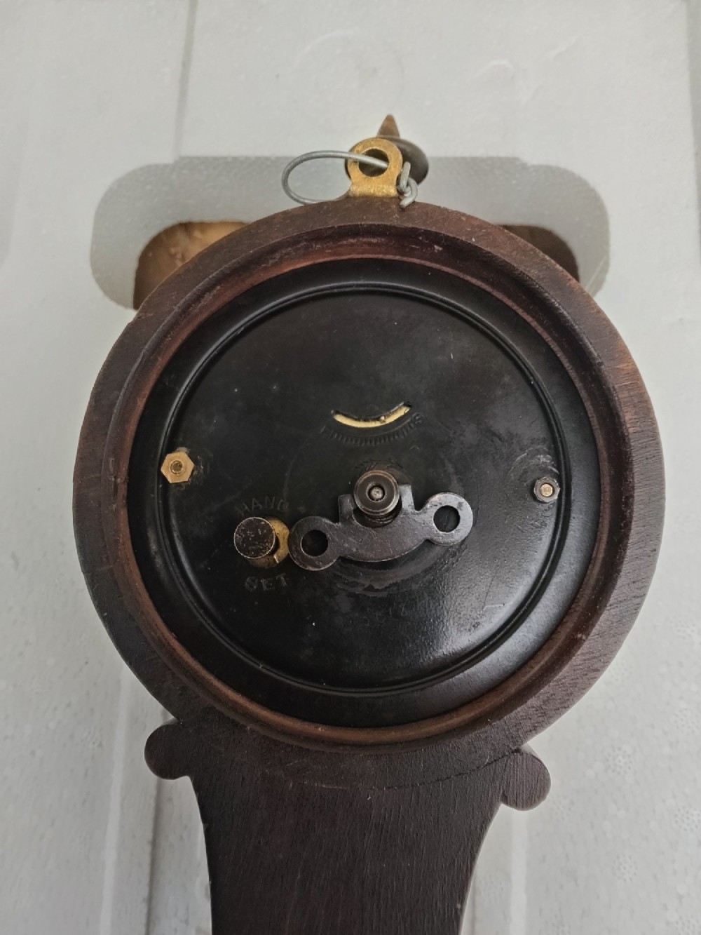 A vertical wooden banjo wall clock featuring a round white dial with black numerals, a narrow waist, and a rectangular lower section with a diamond inlay. View VII