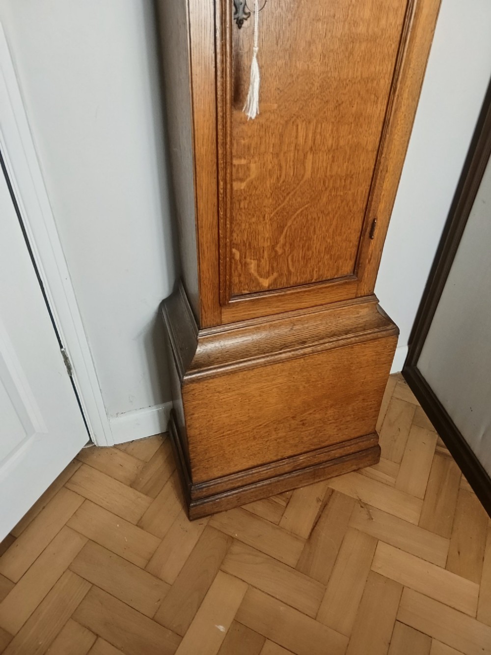 An Early Georgian floor-standing oak longcase clock featuring a carved arch hood, brass dial with strike and silent selector, and a slim trunk door. View V