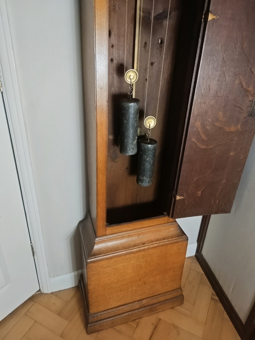 An Early Georgian floor-standing oak longcase clock featuring a carved arch hood, brass dial with strike and silent selector, and a slim trunk door. View VI