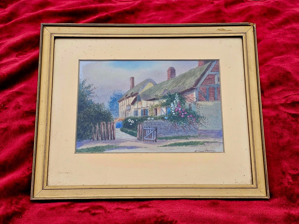 An early 20th-century framed watercolour painting depicting a country cottage with a thatched roof, brickwork, and flowering garden.