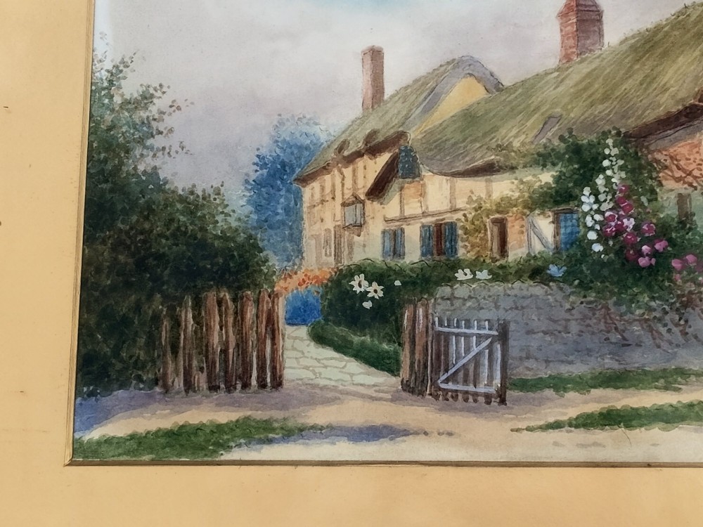 An early 20th-century framed watercolour painting depicting a country cottage with a thatched roof, brickwork, and flowering garden. View V
