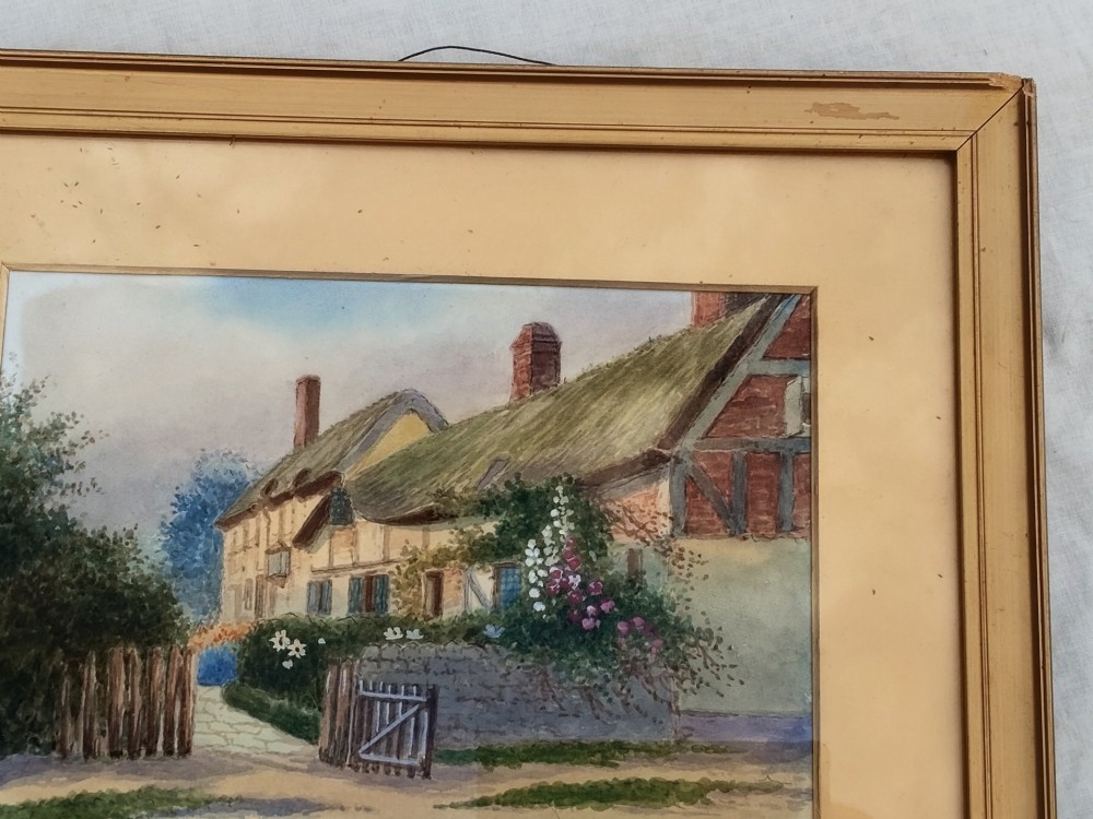An early 20th-century framed watercolour painting depicting a country cottage with a thatched roof, brickwork, and flowering garden. View VI