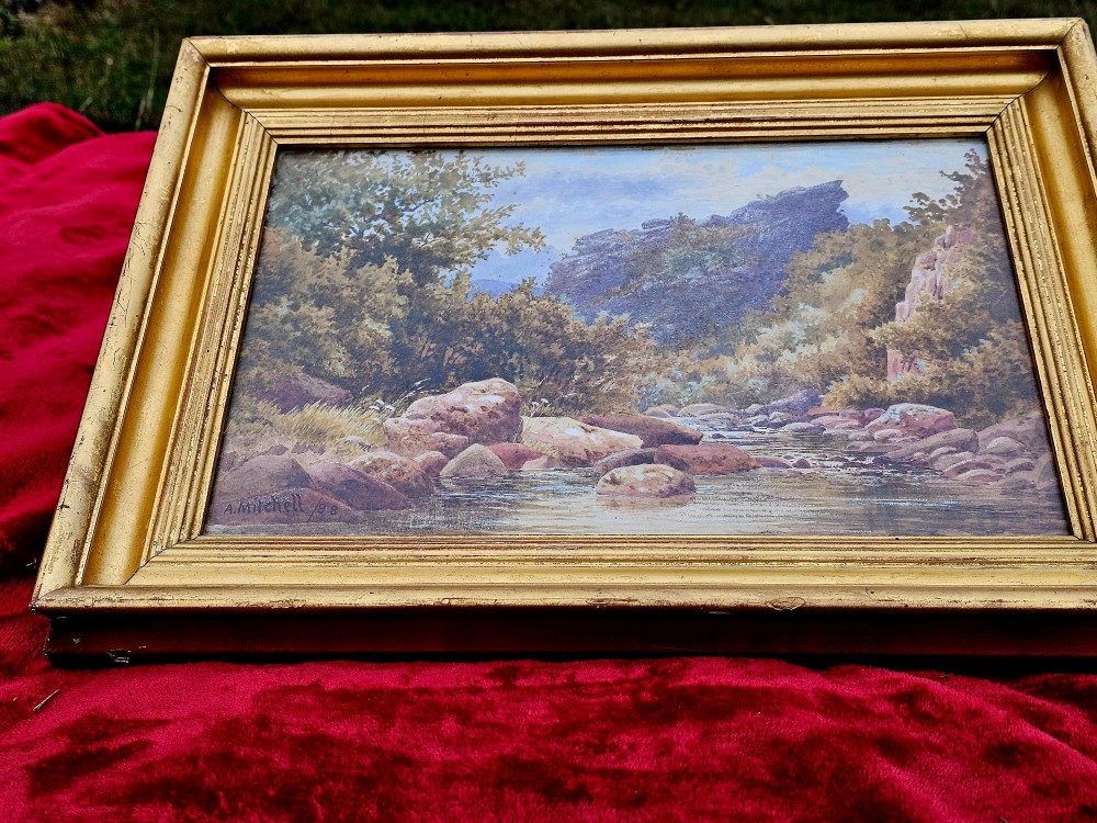 A nineteenth-century watercolour landscape painting depicting a rocky river stream surrounded by foliage, mounted in a moulded gold gilt frame. View II