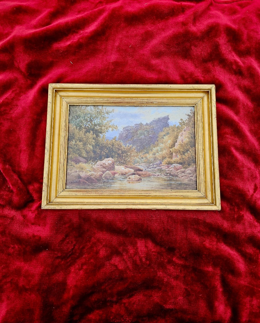 A nineteenth-century watercolour landscape painting depicting a rocky river stream surrounded by foliage, mounted in a moulded gold gilt frame. View IV