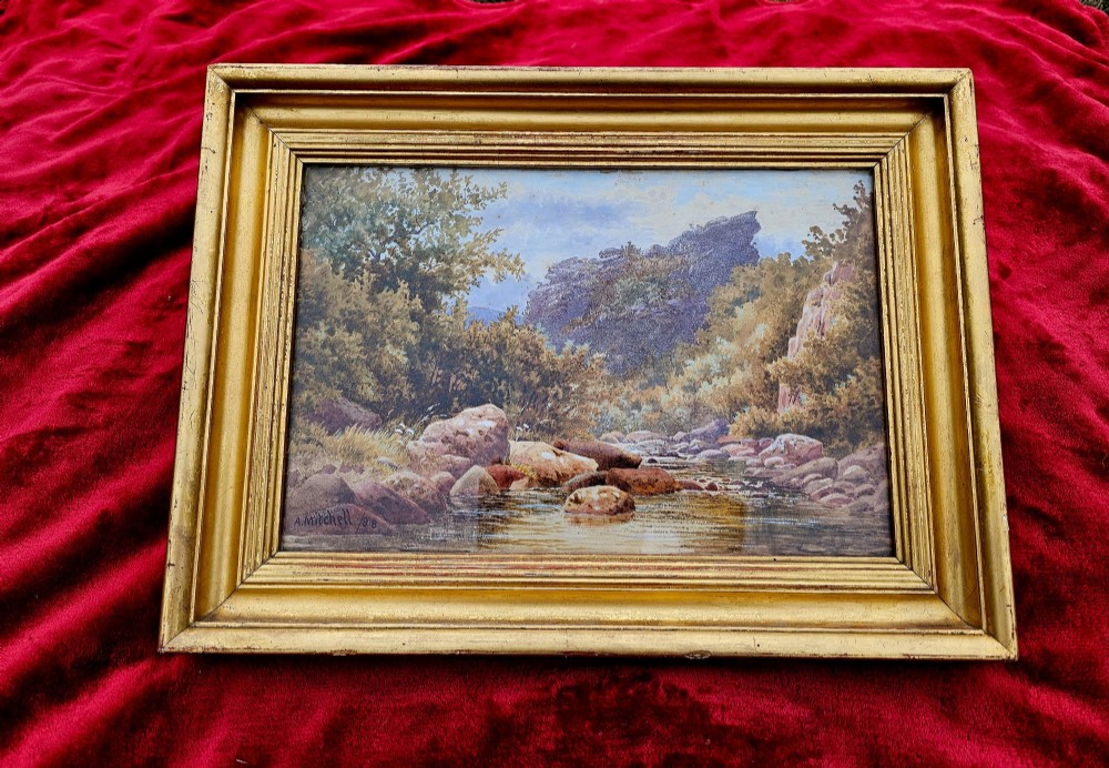 A nineteenth-century watercolour landscape painting depicting a rocky river stream surrounded by foliage, mounted in a moulded gold gilt frame. View V