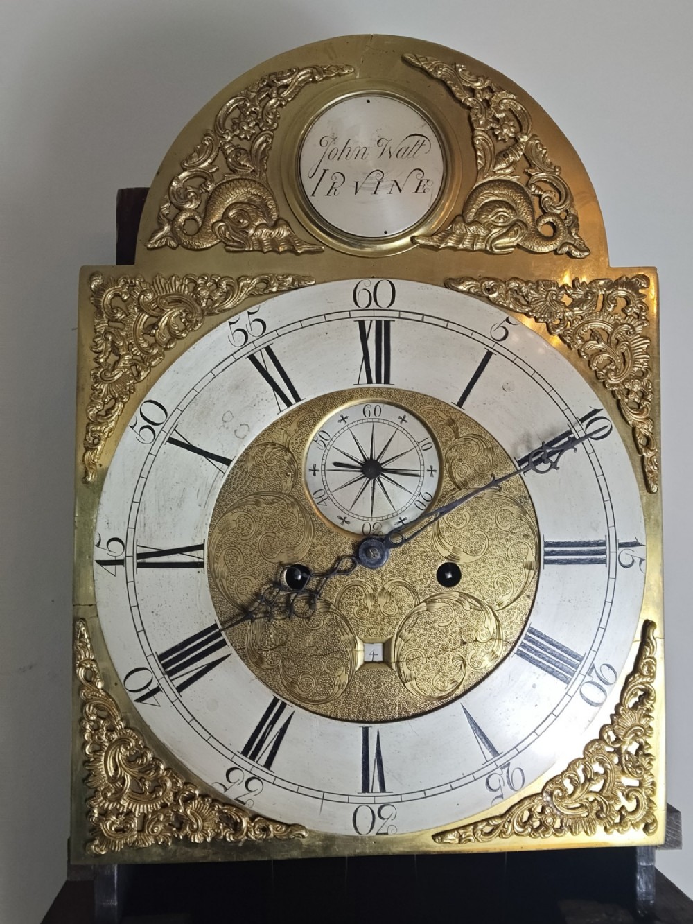 A 19th-century mahogany grandfather clock featuring a swan-neck pediment, brass arch dial, and decorative inlaid paterae on the trunk door. View VI