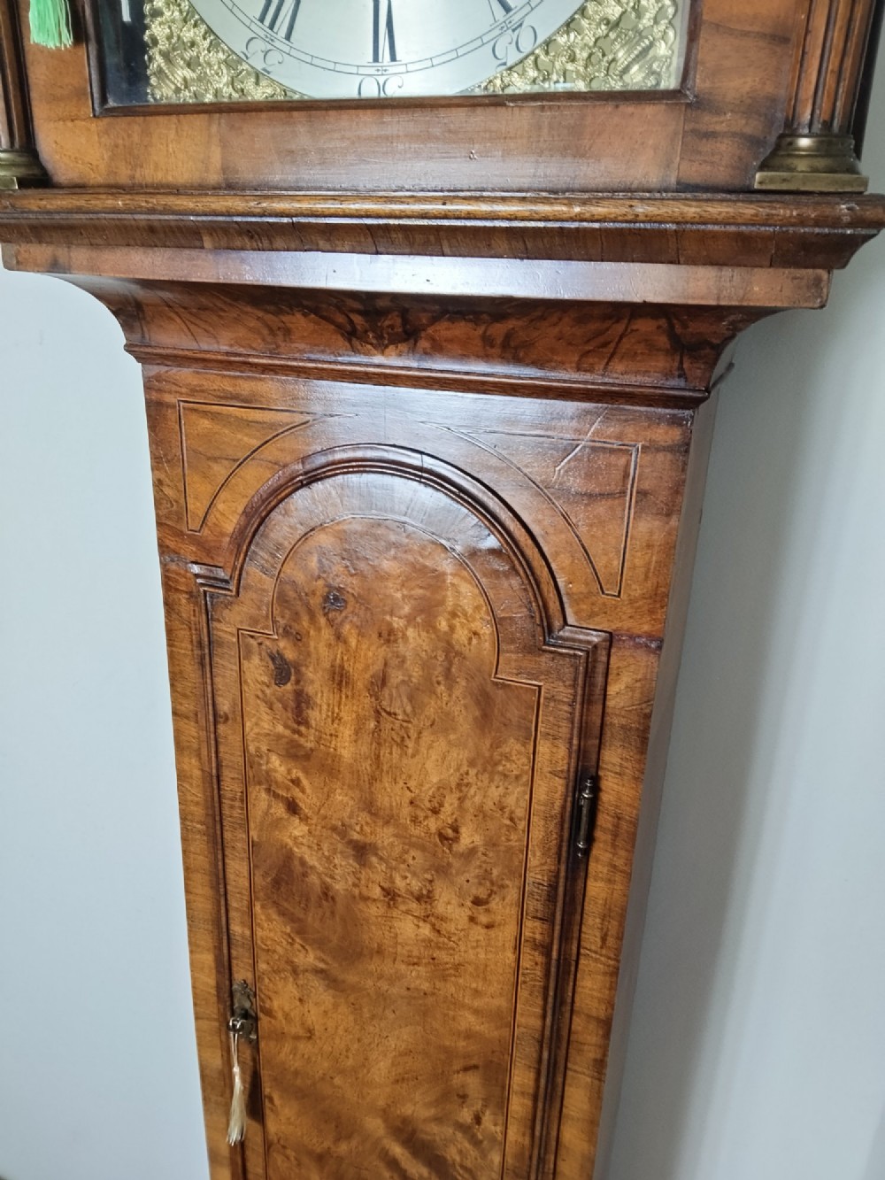 An early Georgian longcase clock featuring a burr walnut veneered case, an arched hood, and a brass dial with Roman numerals. View IV