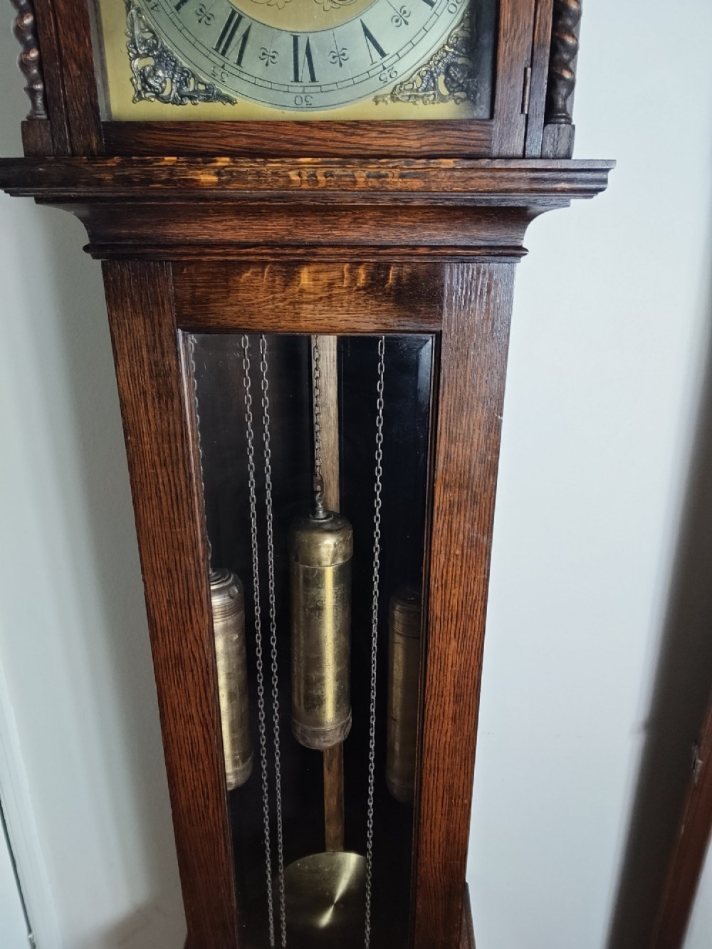 A 1920s dark oak grandmother longcase clock featuring an arched top hood, barley twist columns, brass dial, and glazed door displaying weights. View III