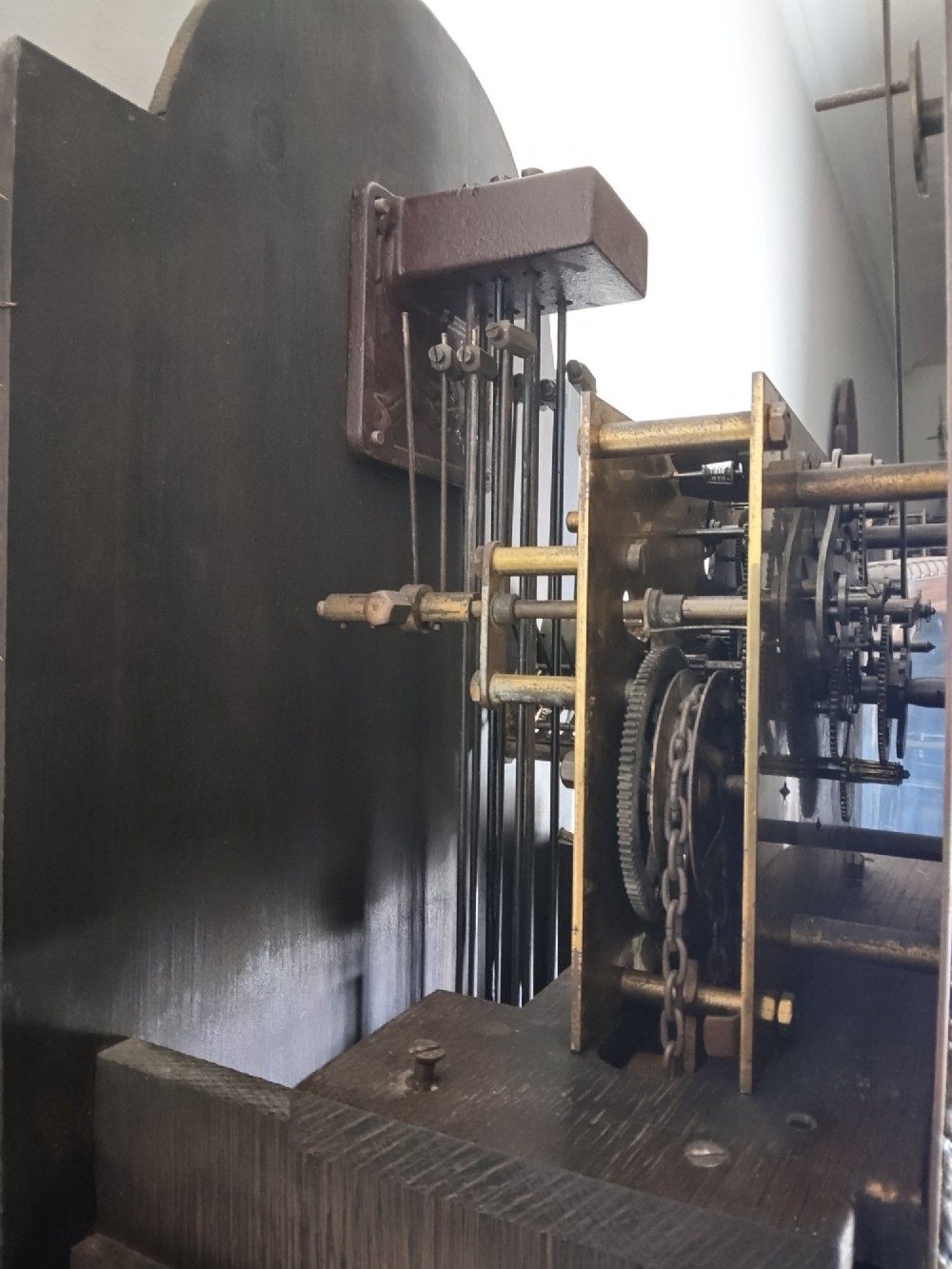 A 1920s dark oak grandmother longcase clock featuring an arched top hood, barley twist columns, brass dial, and glazed door displaying weights. View VII