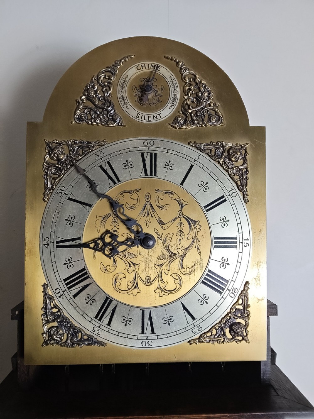 A 1920s dark oak grandmother longcase clock featuring an arched top hood, barley twist columns, brass dial, and glazed door displaying weights. View IX