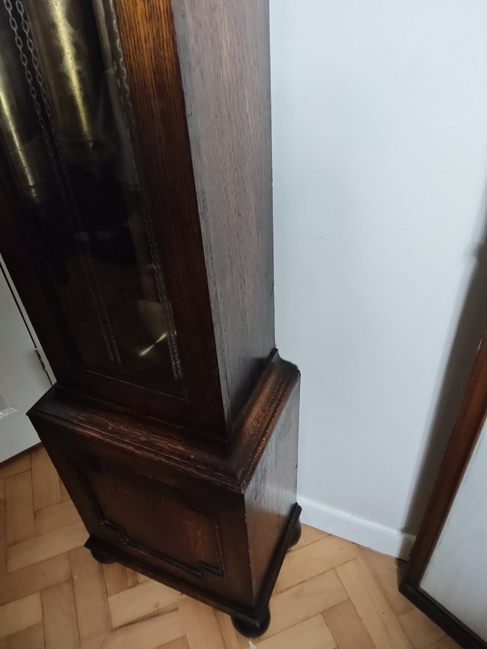 A 1920s dark oak grandmother longcase clock featuring an arched top hood, barley twist columns, brass dial, and glazed door displaying weights. View XIII