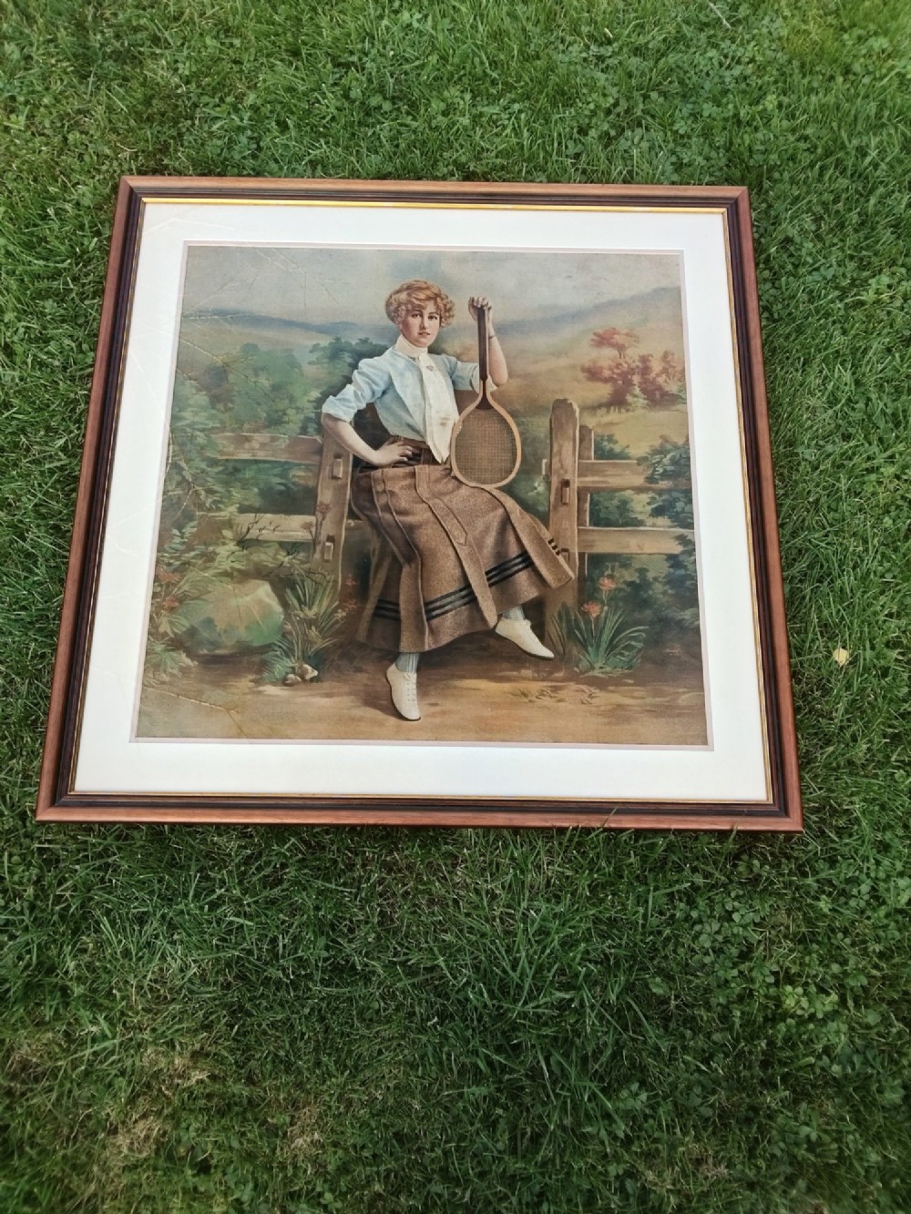 A framed Edwardian tapestry depicting a woman in early twentieth-century sporting attire holding a tennis racket beside a wooden fence. View III