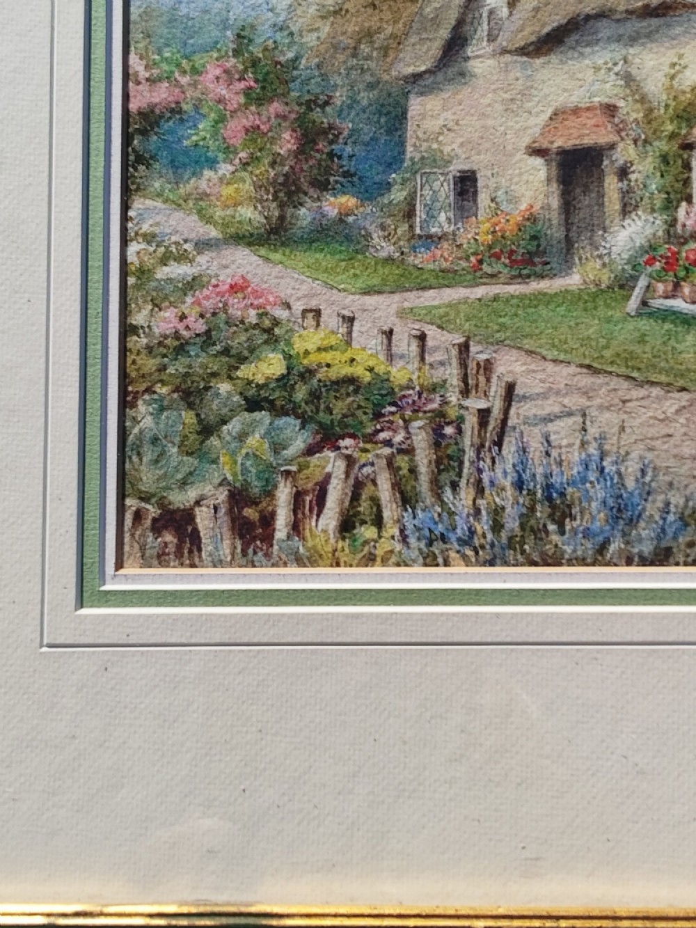 A framed vertical watercolour painting depicting a traditional thatched cottage with a garden filled with colourful flowers under a blue sky. View V