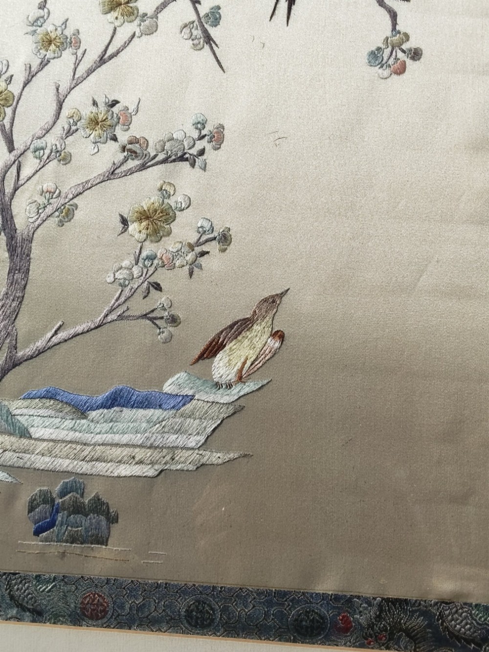 A framed Chinese silk embroidery picture depicting birds perched among blossoming branches and willow leaves on a neutral cream background with a decorative blue brocade border. View III
