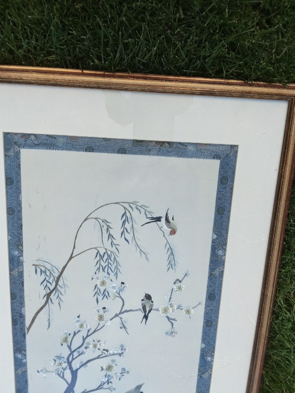 A framed Chinese silk embroidery picture depicting birds perched among blossoming branches and willow leaves on a neutral cream background with a decorative blue brocade border. View IX