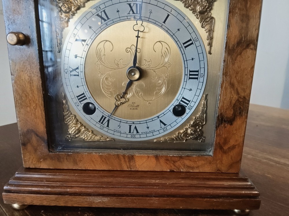 A rectangular burr walnut bracket clock featuring a top brass handle, arched brass dial face with Roman numerals, and a silvered chapter ring. View II