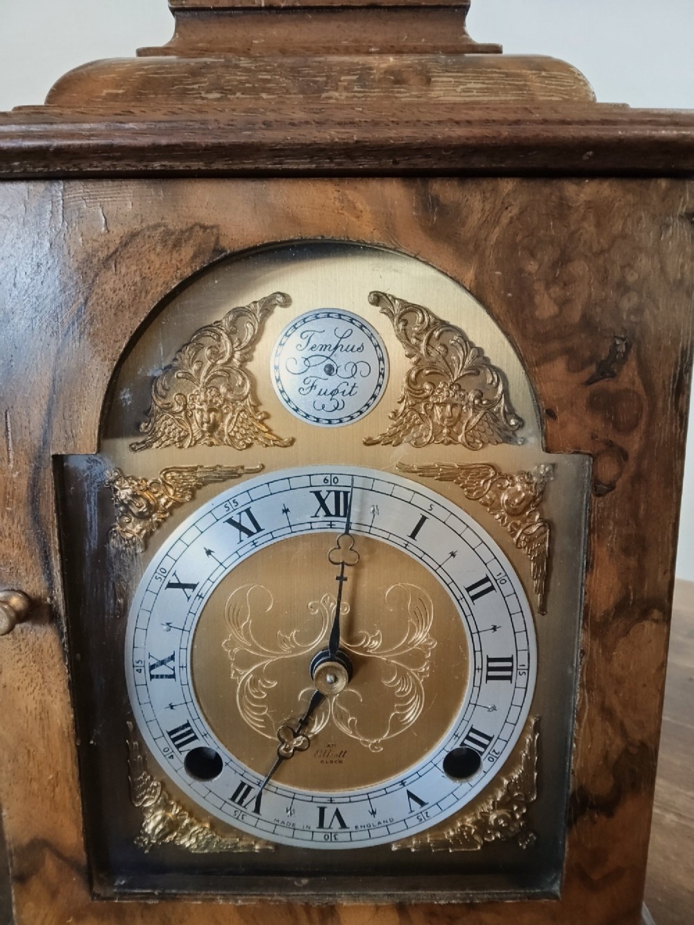 A rectangular burr walnut bracket clock featuring a top brass handle, arched brass dial face with Roman numerals, and a silvered chapter ring. View III